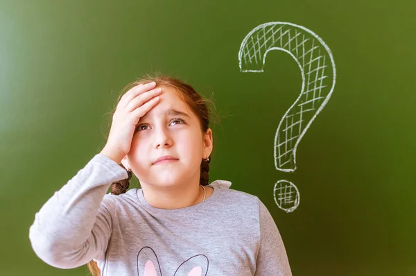 Retrato de una colegiala pensando en resolver un problema en la pizarra durante la lección . — Foto de Stock