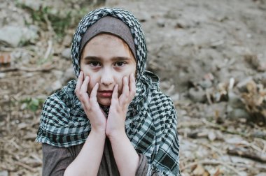 a refugee child in the war, a Muslim girl with a dirty face on the ruins, the concept of peace and war, the child is crying and waiting for help. clipart