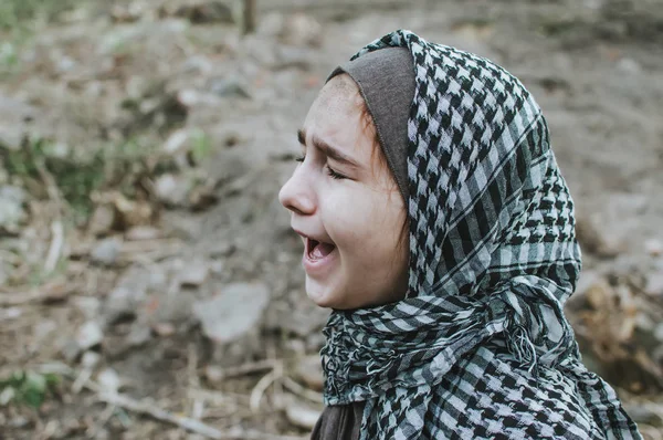 Ett flyktingbarn i kriget, en muslimsk flicka med ett smutsigt ansikte på ruinerna, begreppet fred och krig, barnet gråter och väntar på hjälp. — Stockfoto