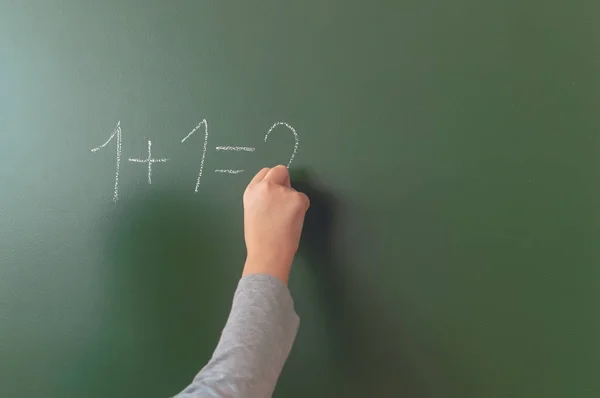 School jongen hand schrijft krijt op een Blackboard tijdens een les op school. — Stockfoto