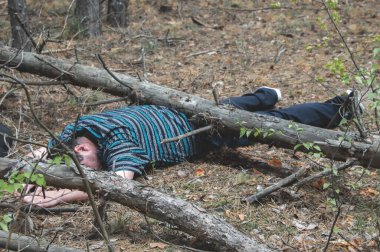 Ormanda bir ceset. Mavi tişörtlü ve pantolonlu ölü bir adam devrilmiş bir ağaç tarafından sıkıştırıldı. Ormandaki kaza kavramı. Yatay fotoğraf.