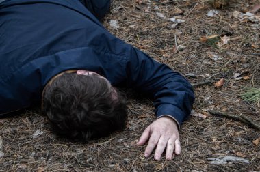 Ormanda cinayet. Mavi gömlekli bir adamın bedeni ormandaki ağaçların arasında yerde yatıyor. Bir saldırı kurbanı. Yatay fotoğraf.