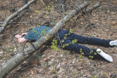 Ormanda bir ceset. Mavi tişörtlü ve pantolonlu ölü bir adam devrilmiş bir ağaç tarafından sıkıştırıldı. Ormandaki kaza kavramı. Yatay fotoğraf.