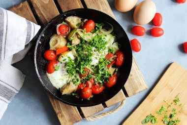 Kızarmış yumurta, kiraz domatesleri, patates ve soğan bir tavada masanın üzerinde duruyor. Kapat..
