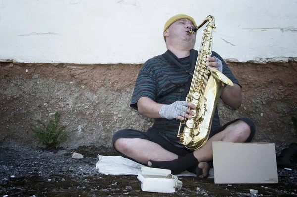 A homeless street musician sits on the street with a saxophone to earn food. Poverty and hunger.