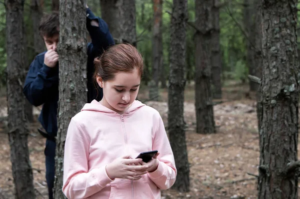 Маніяк Спостерігає Деревом Лісі Дівчиною Підлітком Костюмі Мобільним Телефоном Руках — стокове фото