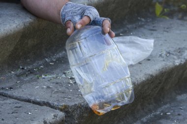 Evsiz bir adamın eldivenli eli boş bir bira şişesinin üzerinde. Yoksulluk, işsizlik, alkolizm. Kapat..