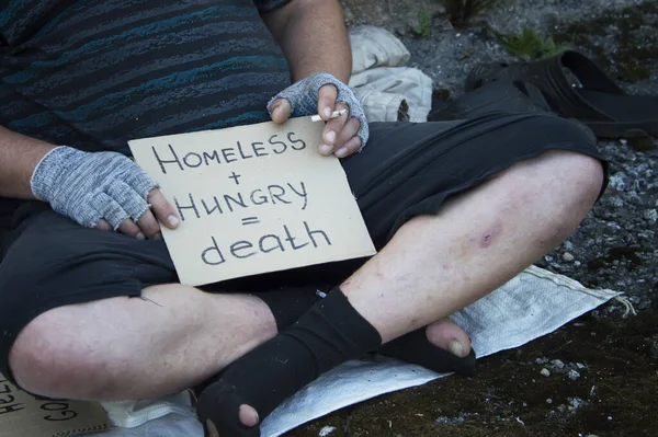 A homeless man sits on the street with a sign and a donation box. Poverty, hunger, unemployment. Close up.