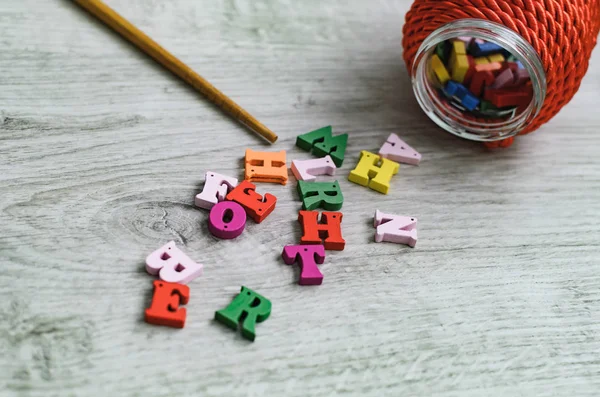 Multicolored letters of the alphabet, container for letters, and a school pointer made of wood on a wooden background.