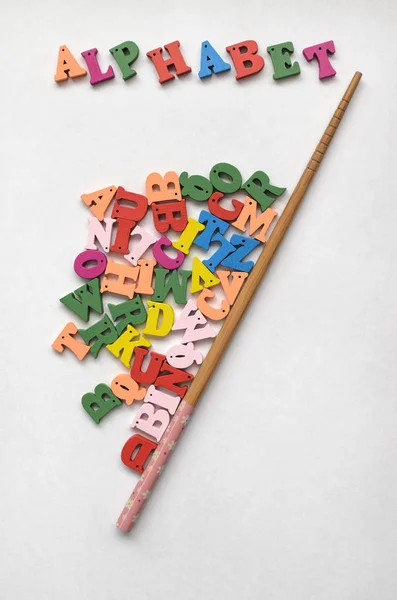 Multicolored letters of the alphabet , the inscription alphabet and a school pointer made of wood on a wooden background.