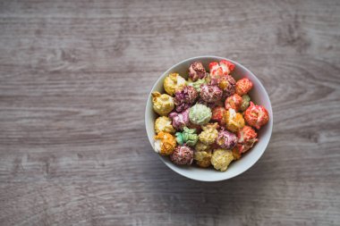 Natürmort şenlikli ruh hali. Bir porselen kase ahşap arka plan üzerinde renkli patlamış mısır.