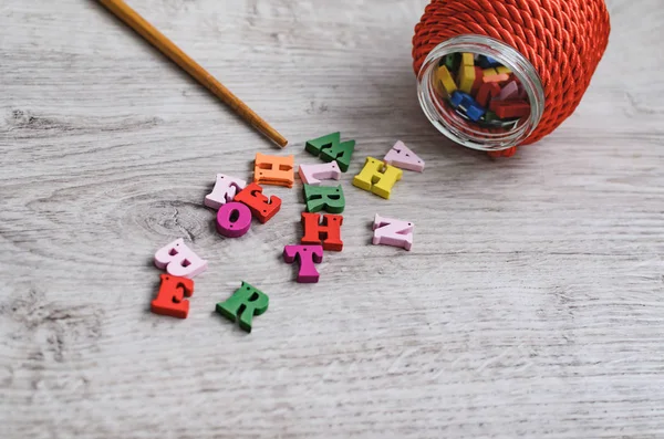 Multicolored letters of the alphabet, container for letters, and a school pointer made of wood on a wooden background.