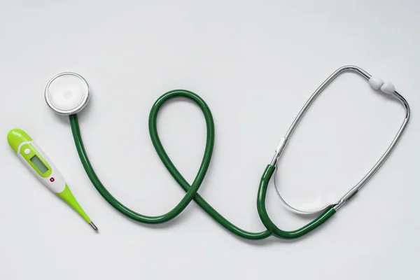 Protecting the health of adults and children, the medical instrument of the doctor pediatrician and the therapist, a green stethoscope and a thermometer on a white background.