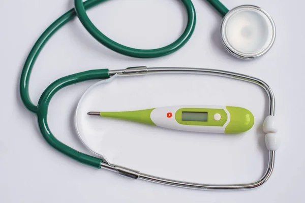 Protecting the health of adults and children, the medical instrument of the doctor pediatrician and the therapist, a green stethoscope and a thermometer on a white background.