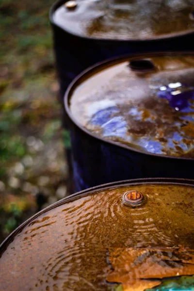 Rainy weather, puddles on rusty old metal barrels, oxidation and destruction of metal by water.