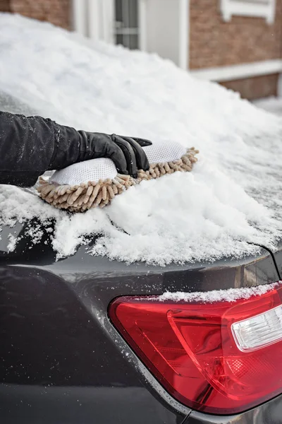 Winter bad weather, blizzard, a man with a soft brush cleans the windows of the car from the snow