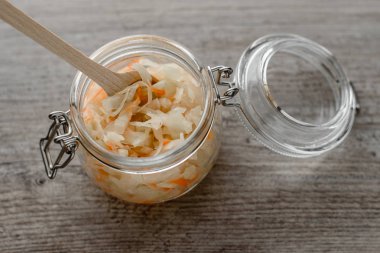 Tahta kaşık ahşap arka plan üzerinde bir cam kavanoza ev yapımı lahana turşusu. Lezzetli mutfak alışveriş