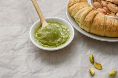 Natürmort fıstık yapıştırın ve kruvasan beyaz plaka, tahta kaşık makarna üzerine hafif bir arka plan için. Yemek ya da kahvaltı için bileşenler.