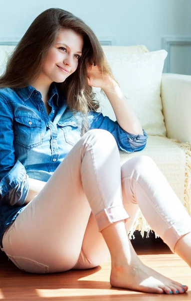 Bella giovane donna seduta sul pavimento del soggiorno vicino al divano — Foto Stock
