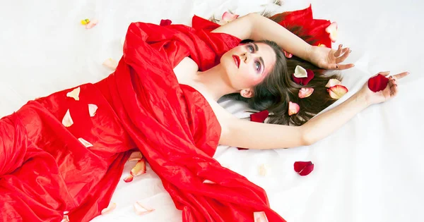 Beautyfull сексуальна дівчина з довгим волоссям, що розслабляється на білих простирадлах з пелюстками троянд — стокове фото