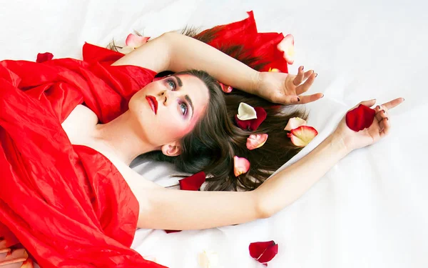 Schöne sexy Mädchen mit langen Haaren entspannen auf weißen Laken mit Rosenblättern — Stockfoto