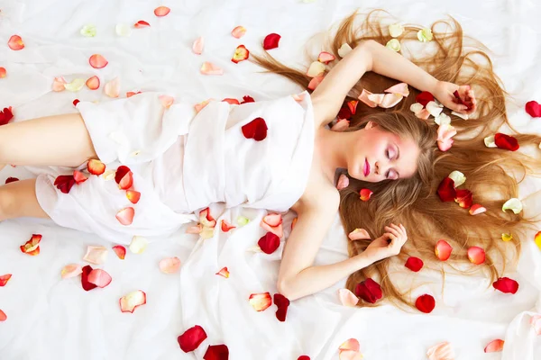 清泉性感女孩与长头发放松在白色床单与玫瑰花瓣 — 图库照片