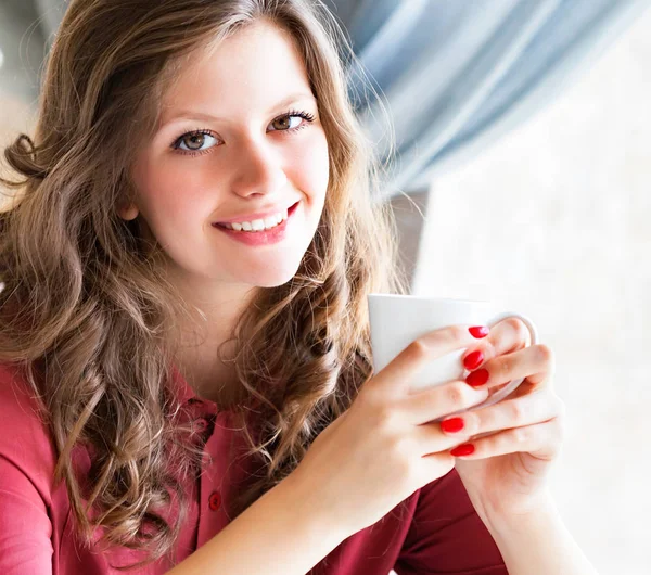 Jonge vrouw een kopje koffie in de hand houden, zitten in een cafe en glimlachen — Stockfoto