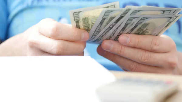 Man counting dollars and filling tax form. He calculating expenses and writing on tax document