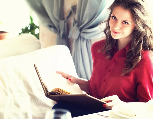 Όμορφη νεαρή γυναίκα ανάγνωση μενού ενώ κάθεται στο εστιατόριο ή καφετέρια — Φωτογραφία Αρχείου