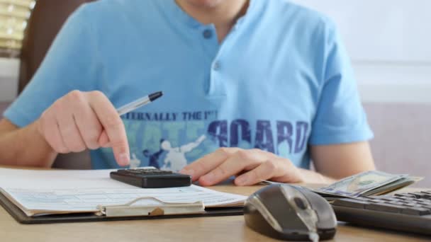 Man in blauw T-shirt tellen dollar en belastingformulier vullen — Stockvideo