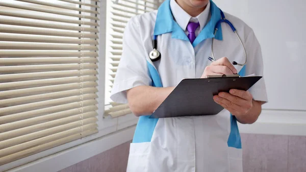 A doctor filling up medical form on a clipboard, closeup. Healthcare, insurance and medicine concept.