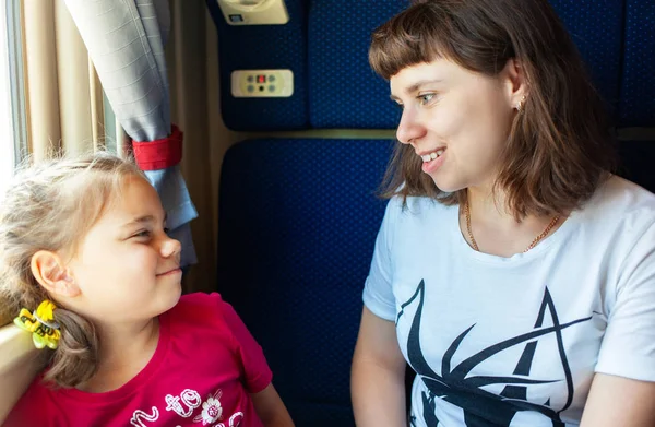 電車の中で窓を通して見ている小さな女の子と彼女の母親. — ストック写真