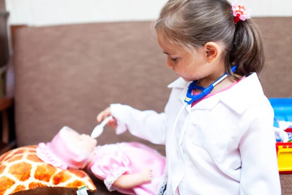 Cute child girl playing doctor with baby doll toy