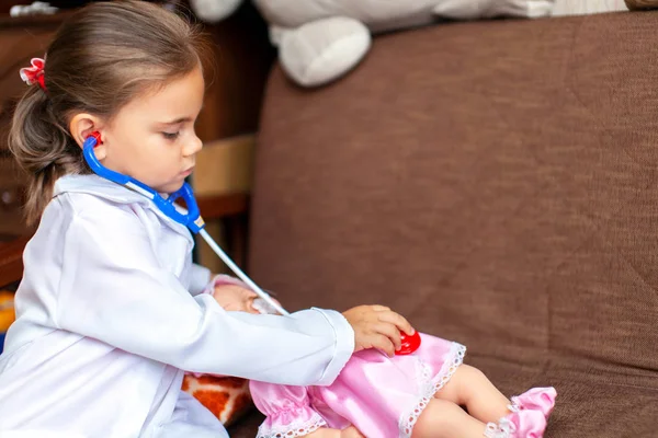 Cute child girl playing doctor with baby doll toy