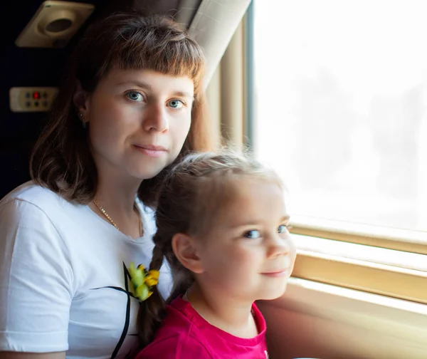 電車の中で窓を通して見ている小さな女の子と彼女の母親. — ストック写真