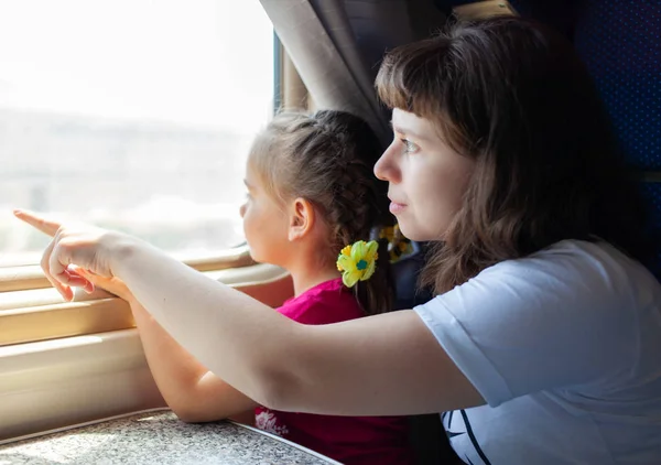 電車の中で窓を通して見ている小さな女の子と彼女の母親. — ストック写真