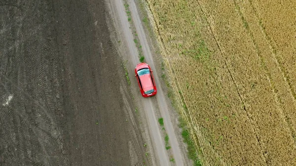 Blick von oben auf ein Feld mit Weizen und einem roten Auto, das sich auf der Landstraße bewegt. — Stockfoto