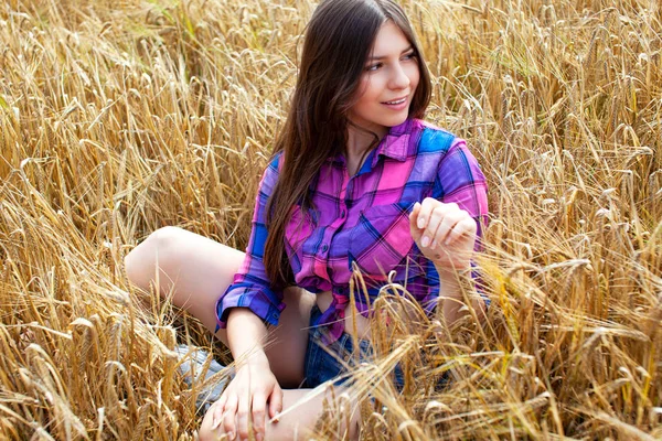 Young country woman in plaid shirt possing in a field of wheat