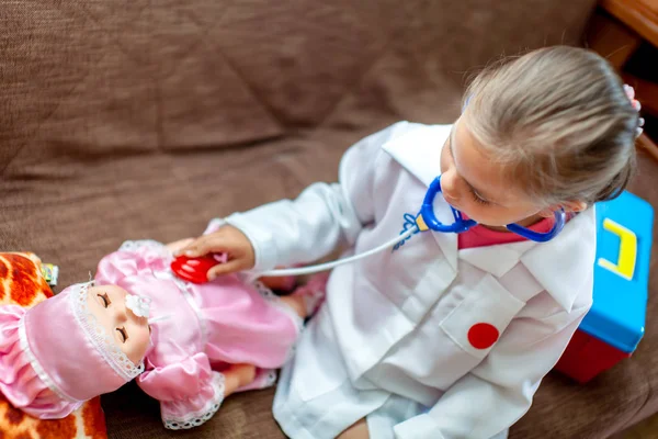 Cute child girl playing doctor with baby doll toy