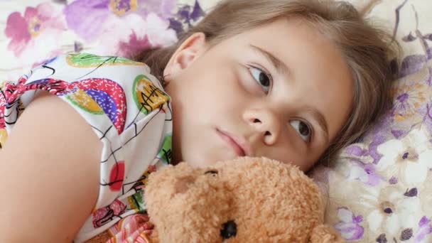 Upset sick child girl lying on a bed — Stock Video