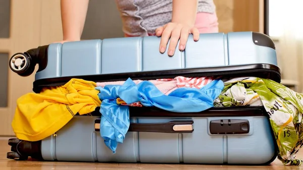 Young woman trying to pack overfilled suitcase