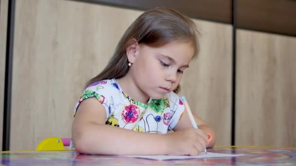 Una niña o un niño de escuela primaria lindo pintar o escribir en papel . — Vídeo de stock