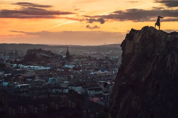 Kayanın üzerinde duran ve yukarıdan bir gün batımı şehre, Edinburgh, İskoçya, Birleşik Krallık arayan bir kız kontur