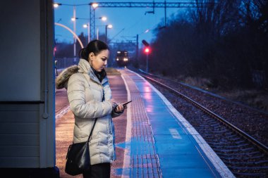 Bir kadın bir tren wating ve geceleri, Glasgow, İskoçya bir demiryolu ve akılda kalıcı bir trenin arka plan üzerinde bir tren istasyonunda bir akıllı telefon kullanır. Bu fotoğraf için izin verildi.