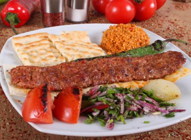 Yulaf, domates ve yeşille kaplı bir tabakta Adana barbekü servisi