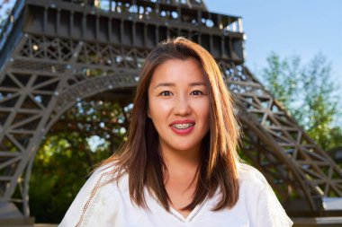 Beyaz tişörtlü Asyalı kız kameraya bakıyor ve gülümsüyor, geçmişi bulanık.