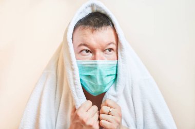 Tıbbi maskeli bir adam, üzerini sabahlıkla örttü. Kendini izole etti, karantinaya aldı. Evde kaldı, korktu.                               