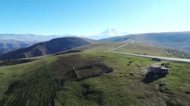 Yukarıdaki dağ manzarası: karlı zirveler, küçük bir ev ve yolda atlar için bir ağıl, Elbrus bölgesi, Rusya