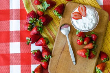 Sağlıklı meyve naziklerdi küçük cam kase, Olgun çilek ve ahşap kesme tahtası ve sarı mutfak havlusu tatlı kaşığı taze yoğurt ile