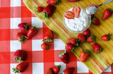 Sağlıklı yaz naziklerdi küçük cam kase, Olgun çilek ve ahşap kesme tahtası ve sarı mutfak havlusu tatlı kaşığı taze yoğurt ile